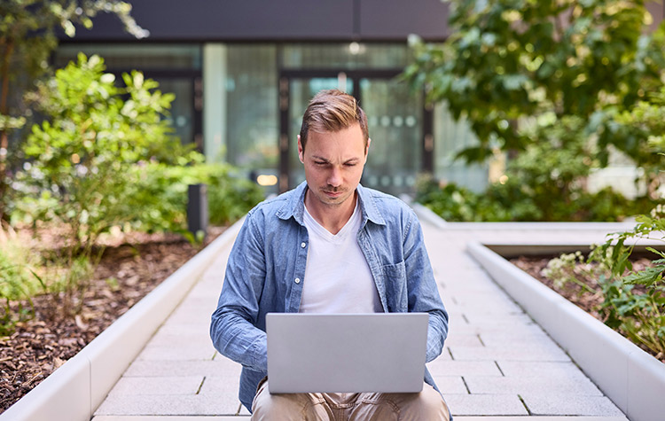Young employee sitting in the courtyard in front of his laptop
